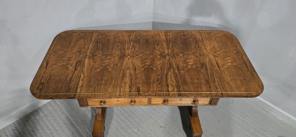 A Regency rosewood sofa table with two frieze drawers, brass line inlay, drop leaves, carved rosette corners, and reeded legs on brass castors. View XXII
