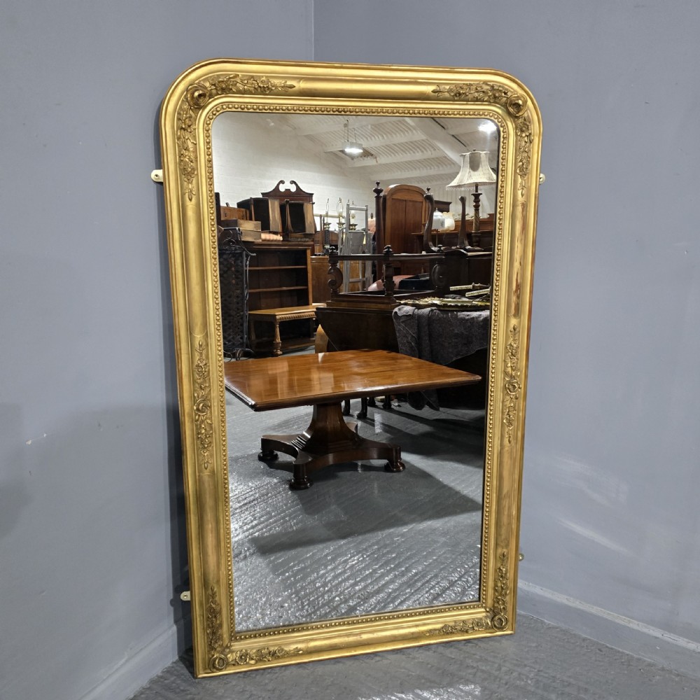 A large rectangular antique giltwood pier mirror featuring rounded top corners, beaded inner borders, and floral relief moulding along the gold frame.
