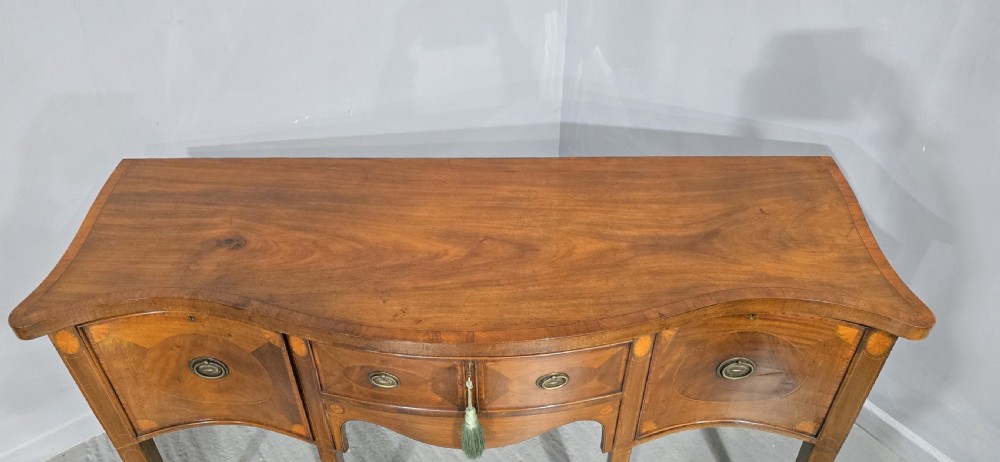 An Edwardian mahogany sideboard featuring satinwood inlay, oval fan motifs, central drawers, flanking cupboards, and slender tapered legs. View VIII
