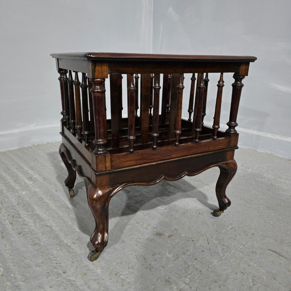 A dark rosewood Victorian Canterbury featuring turned spindle sides, vertical dividers, a flat top surface, and cabriole legs on brass castors. View II