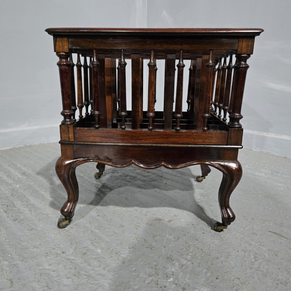 A dark rosewood Victorian Canterbury featuring turned spindle sides, vertical dividers, a flat top surface, and cabriole legs on brass castors. View III