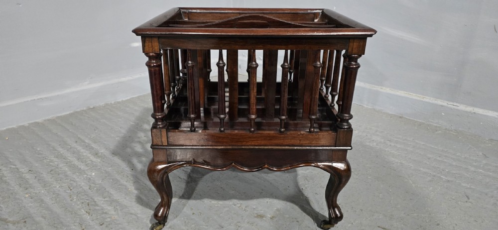 A dark rosewood Victorian Canterbury featuring turned spindle sides, vertical dividers, a flat top surface, and cabriole legs on brass castors. View V