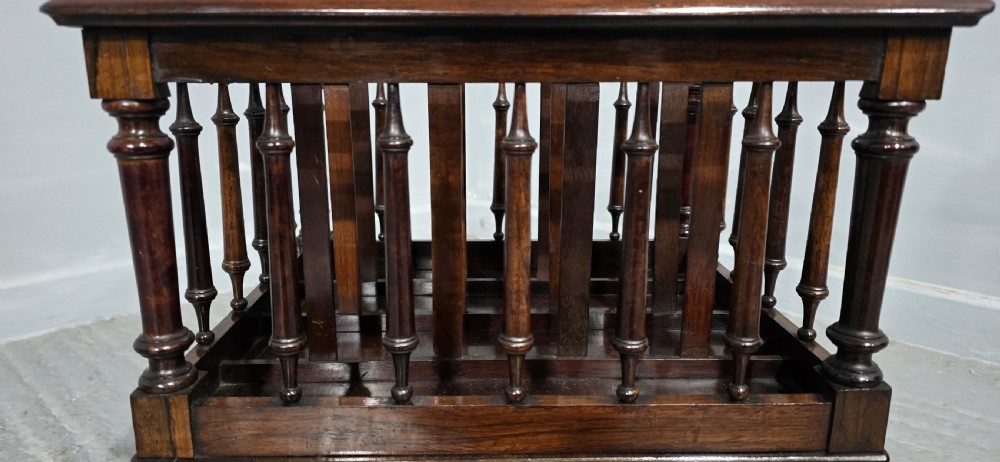 A dark rosewood Victorian Canterbury featuring turned spindle sides, vertical dividers, a flat top surface, and cabriole legs on brass castors. View VII