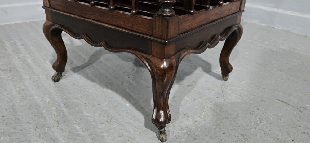 A dark rosewood Victorian Canterbury featuring turned spindle sides, vertical dividers, a flat top surface, and cabriole legs on brass castors. View IX