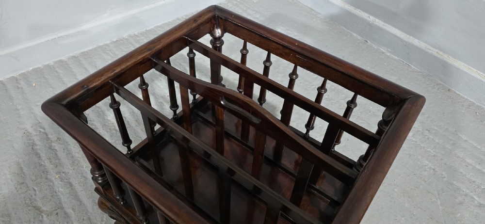 A dark rosewood Victorian Canterbury featuring turned spindle sides, vertical dividers, a flat top surface, and cabriole legs on brass castors. View X