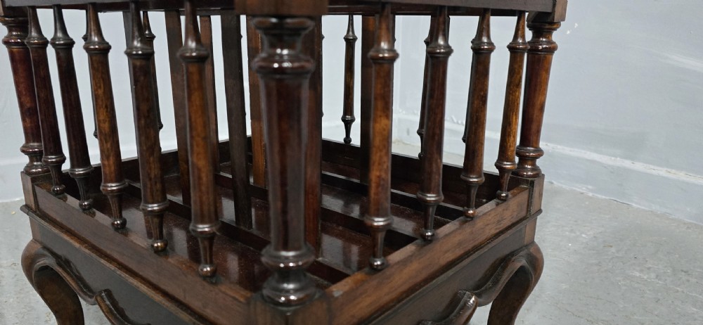 A dark rosewood Victorian Canterbury featuring turned spindle sides, vertical dividers, a flat top surface, and cabriole legs on brass castors. View XII