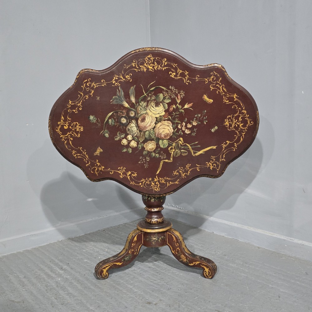 An Italian painted tilt-top side table featuring a dark burgundy ground decorated with a central hand-painted floral bouquet and gilt scrollwork borders.