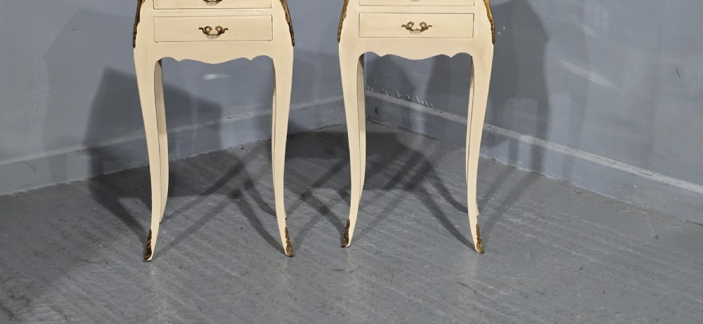 A pair of slender cream-painted French Louis style bedside chests featuring shaped marble tops, three drawers, and decorative brass mounts on tall cabriole legs. View II