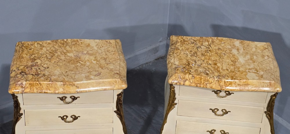A pair of slender cream-painted French Louis style bedside chests featuring shaped marble tops, three drawers, and decorative brass mounts on tall cabriole legs. View VI