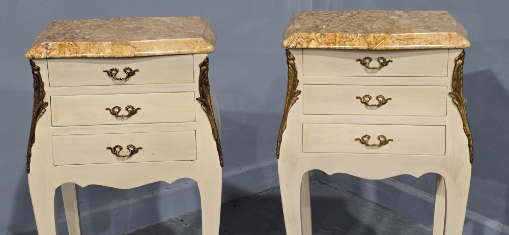 A pair of slender cream-painted French Louis style bedside chests featuring shaped marble tops, three drawers, and decorative brass mounts on tall cabriole legs. View VII