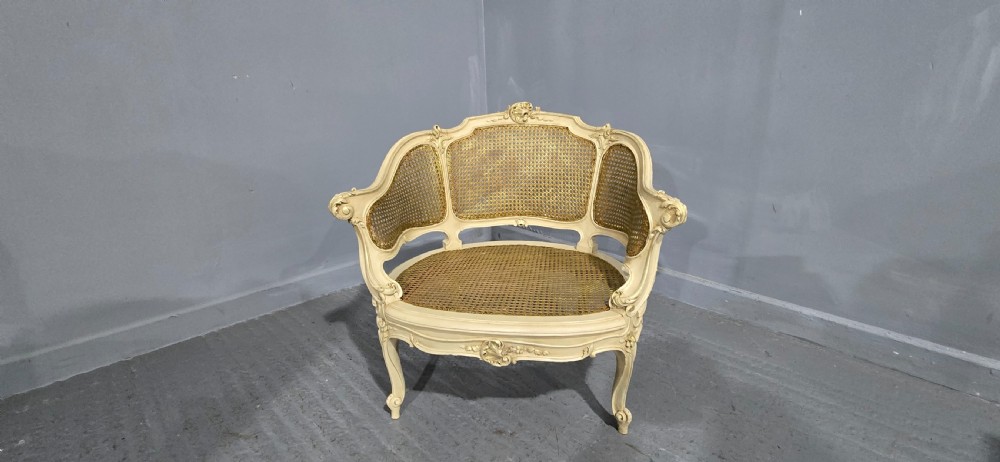 A French Louis XV style cream painted and gilded tub armchair featuring a carved wooden frame with hand-woven rattan cane back, sides, and seat on cabriole legs. View II