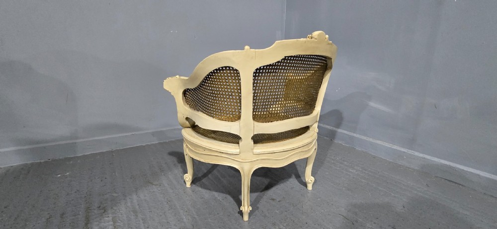 A French Louis XV style cream painted and gilded tub armchair featuring a carved wooden frame with hand-woven rattan cane back, sides, and seat on cabriole legs. View IV