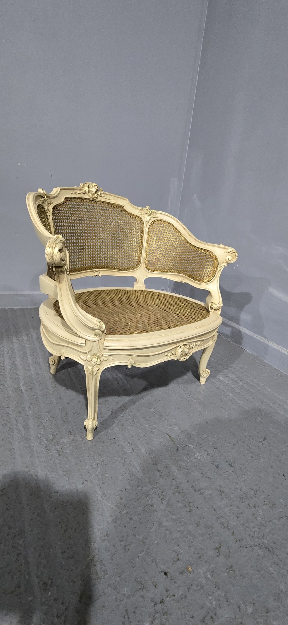 A French Louis XV style cream painted and gilded tub armchair featuring a carved wooden frame with hand-woven rattan cane back, sides, and seat on cabriole legs. View VII