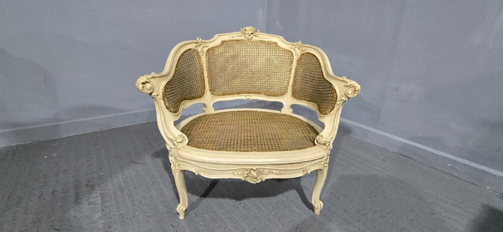 A French Louis XV style cream painted and gilded tub armchair featuring a carved wooden frame with hand-woven rattan cane back, sides, and seat on cabriole legs. View VIII