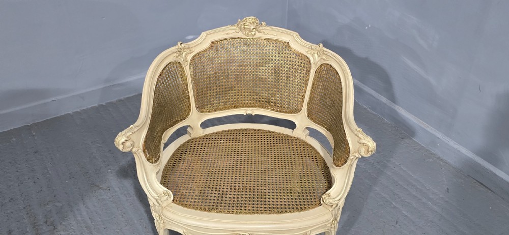 A French Louis XV style cream painted and gilded tub armchair featuring a carved wooden frame with hand-woven rattan cane back, sides, and seat on cabriole legs. View IX