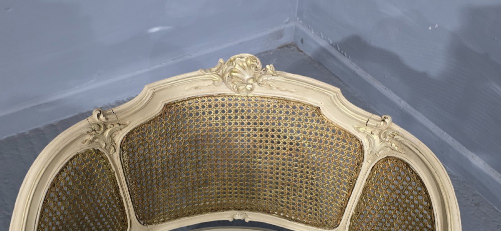 A French Louis XV style cream painted and gilded tub armchair featuring a carved wooden frame with hand-woven rattan cane back, sides, and seat on cabriole legs. View X