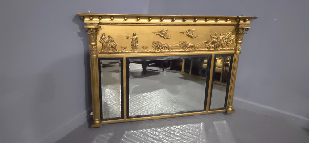 A Regency giltwood triptych overmantel mirror featuring a classical bas-relief frieze above three mirrored panels separated by ebonised slips and framed by fluted Corinthian columns. View II