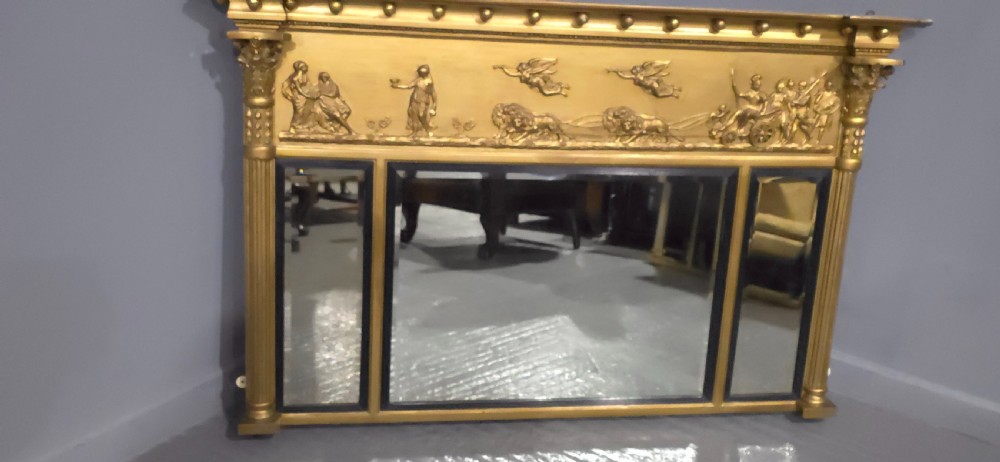 A Regency giltwood triptych overmantel mirror featuring a classical bas-relief frieze above three mirrored panels separated by ebonised slips and framed by fluted Corinthian columns. View III