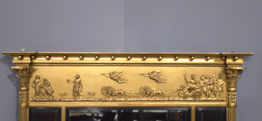 A Regency giltwood triptych overmantel mirror featuring a classical bas-relief frieze above three mirrored panels separated by ebonised slips and framed by fluted Corinthian columns. View IV