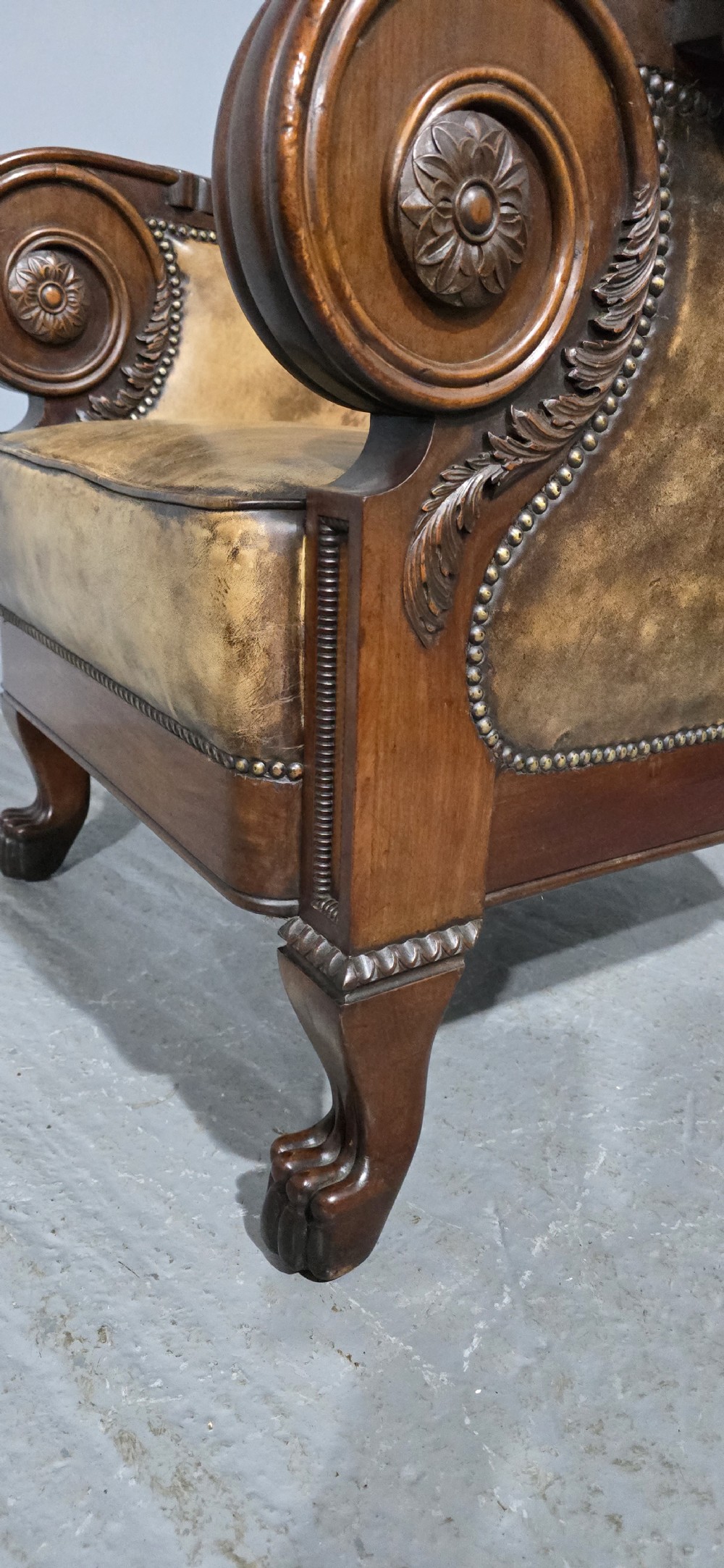 A Regency mahogany library armchair upholstered in aged tan leather featuring carved scroll arms, brass studding, and carved paw feet. View V