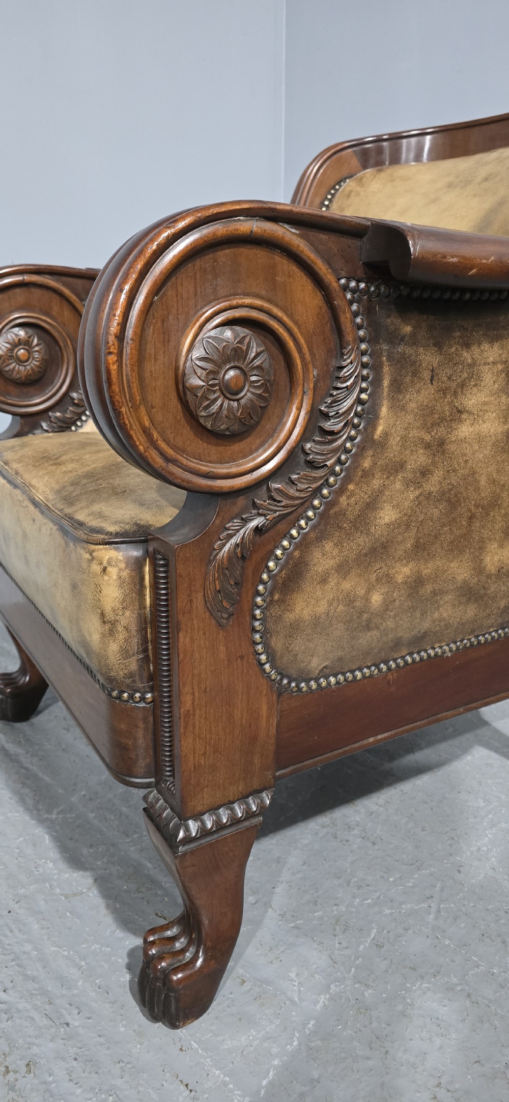 A Regency mahogany library armchair upholstered in aged tan leather featuring carved scroll arms, brass studding, and carved paw feet. View VI