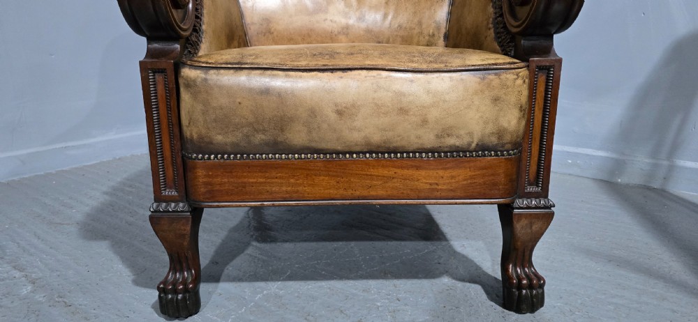 A Regency mahogany library armchair upholstered in aged tan leather featuring carved scroll arms, brass studding, and carved paw feet. View VIII