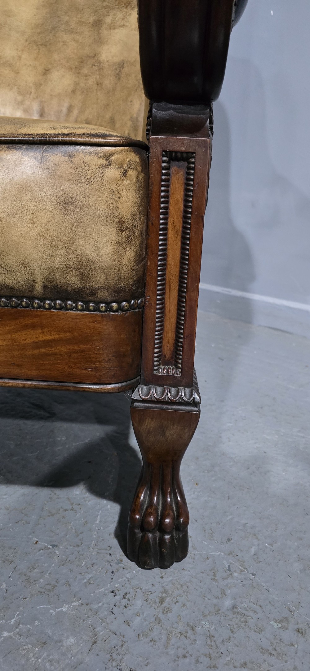 A Regency mahogany library armchair upholstered in aged tan leather featuring carved scroll arms, brass studding, and carved paw feet. View IX