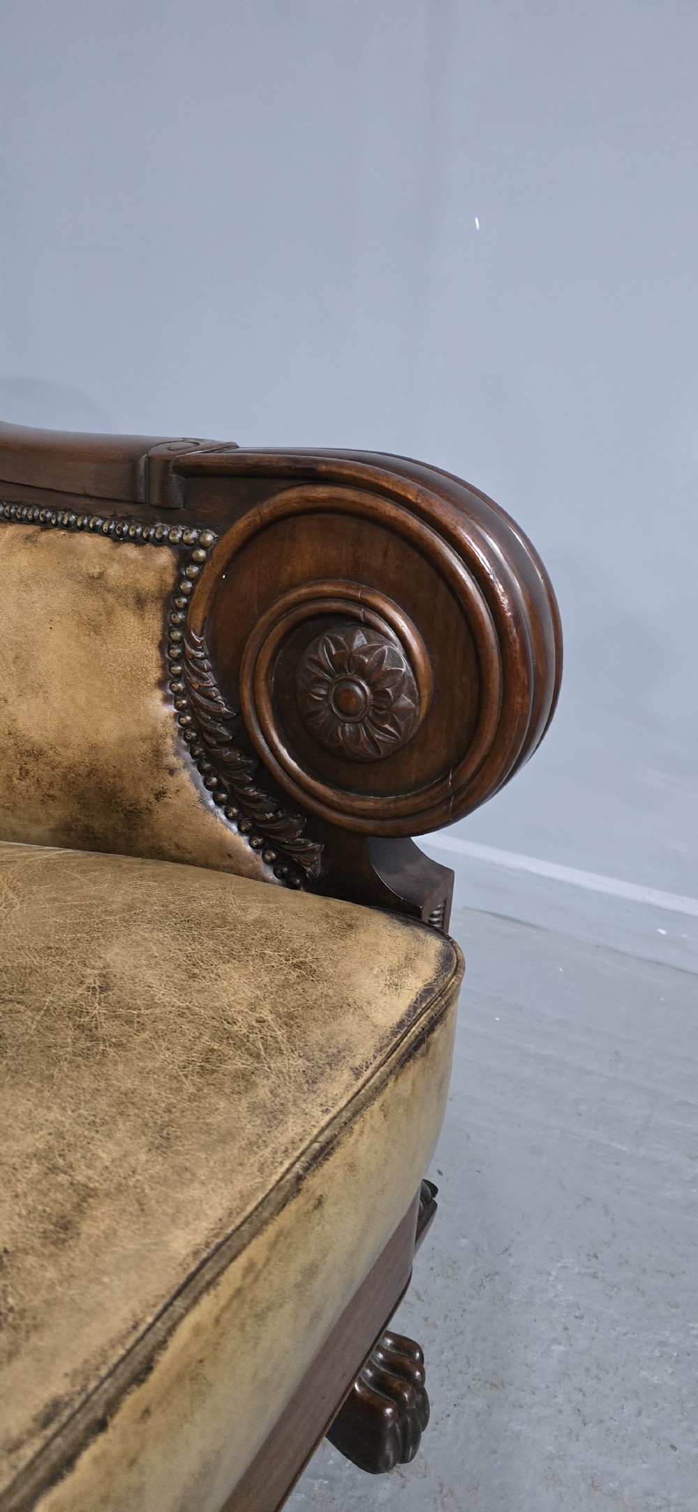 A Regency mahogany library armchair upholstered in aged tan leather featuring carved scroll arms, brass studding, and carved paw feet. View XI