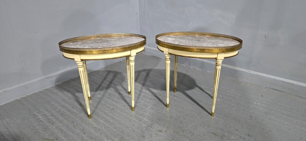 A pair of oval cream-painted French side tables featuring grey-veined marble tops, pierced brass galleries, and fluted tapered legs. View II