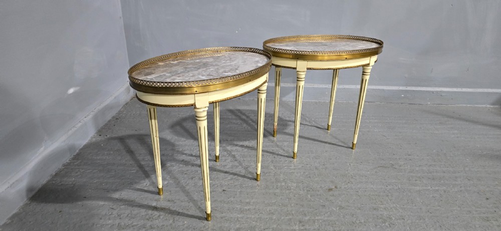A pair of oval cream-painted French side tables featuring grey-veined marble tops, pierced brass galleries, and fluted tapered legs. View IV