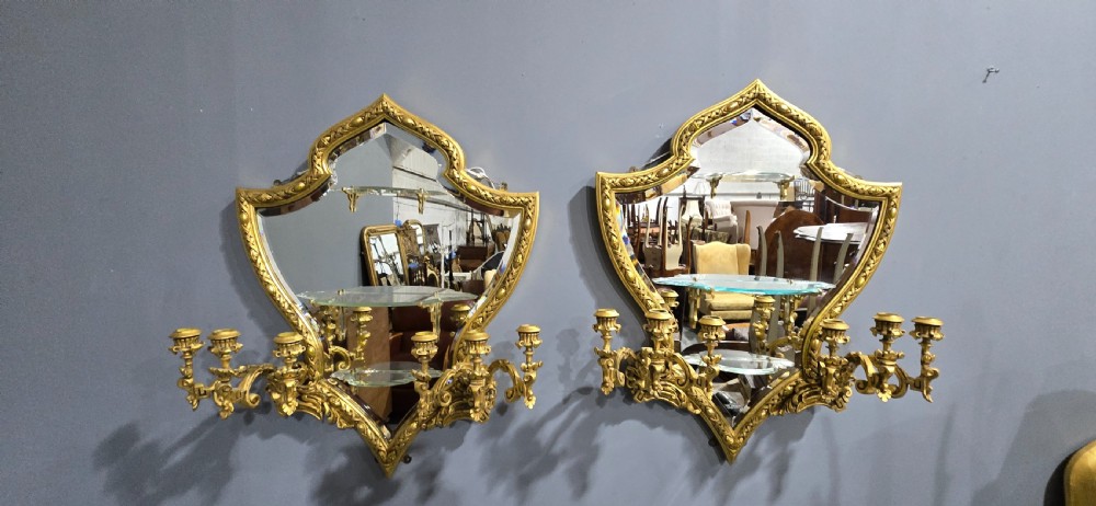 A pair of shaped giltwood girandole wall mirrors featuring ornate carved frames, integrated glass shelves, and multi-branch candle sconces. View III