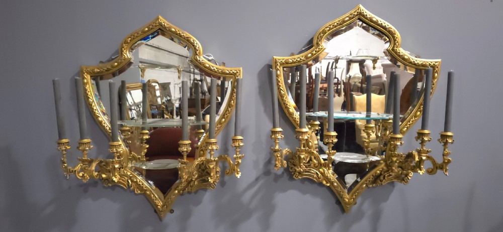 A pair of shaped giltwood girandole wall mirrors featuring ornate carved frames, integrated glass shelves, and multi-branch candle sconces. View V