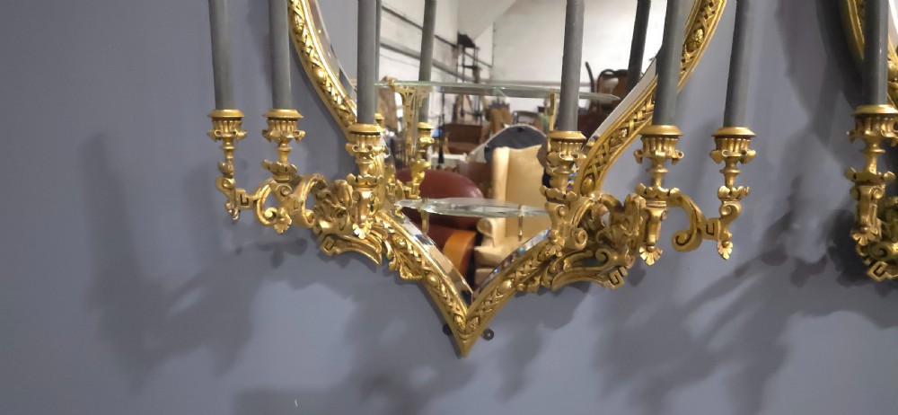 A pair of shaped giltwood girandole wall mirrors featuring ornate carved frames, integrated glass shelves, and multi-branch candle sconces. View VI