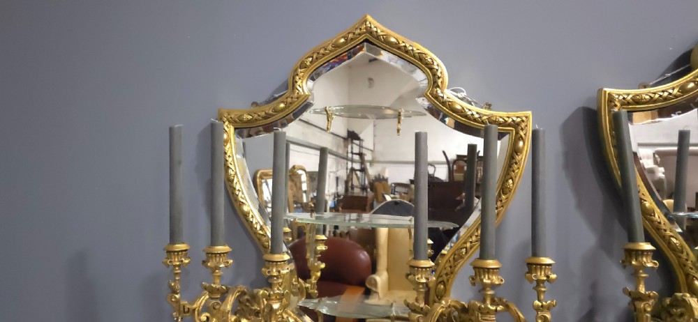 A pair of shaped giltwood girandole wall mirrors featuring ornate carved frames, integrated glass shelves, and multi-branch candle sconces. View VII