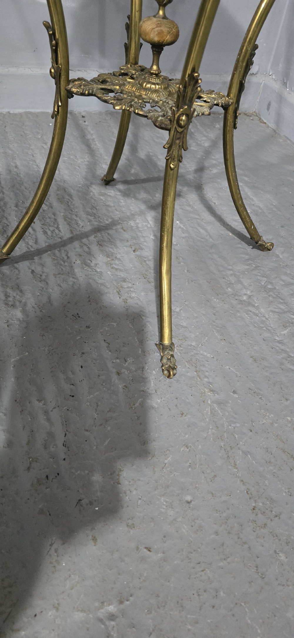 An ornate tall brass plant stand featuring a square white marble top, detailed mask motifs, curved legs, and a lower decorative tier. View VI