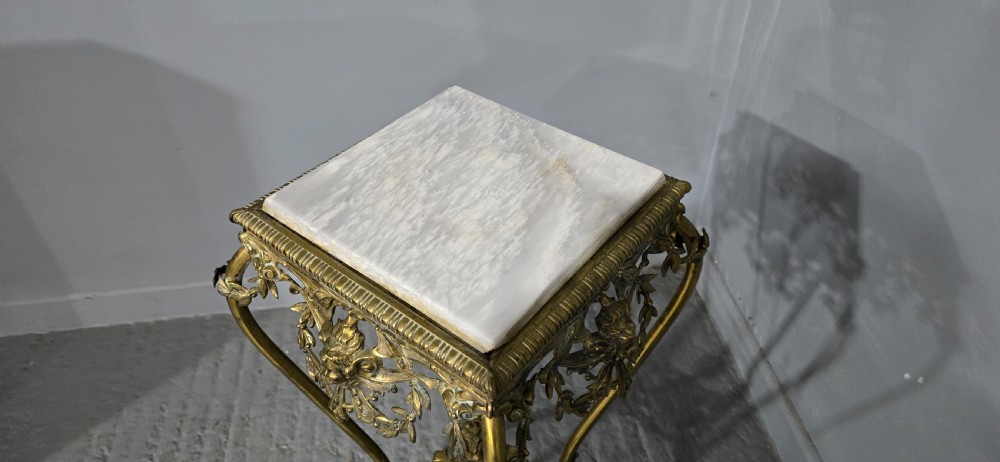 An ornate tall brass plant stand featuring a square white marble top, detailed mask motifs, curved legs, and a lower decorative tier. View VIII