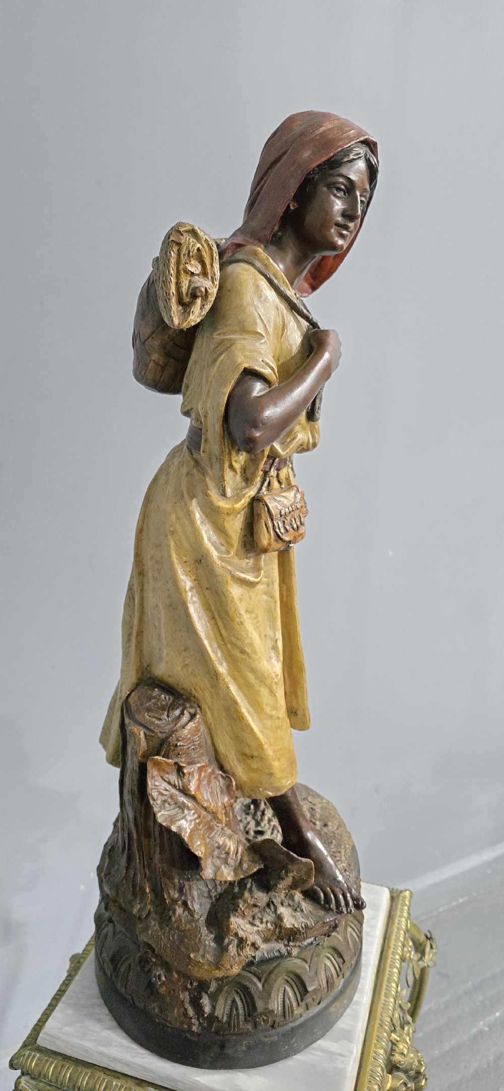 A polychrome terracotta sculpture depicting a standing woman dressed as a fisher girl carrying a basket on her back and holding fish. View IV