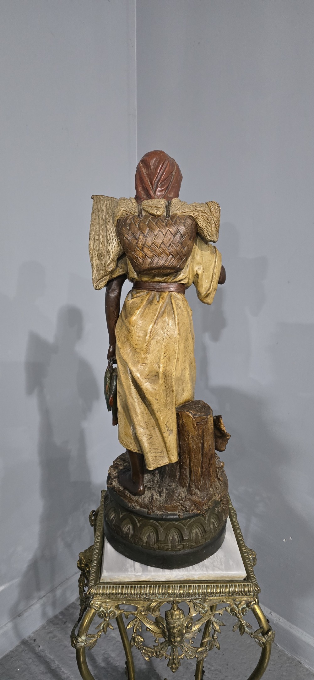 A polychrome terracotta sculpture depicting a standing woman dressed as a fisher girl carrying a basket on her back and holding fish. View VI