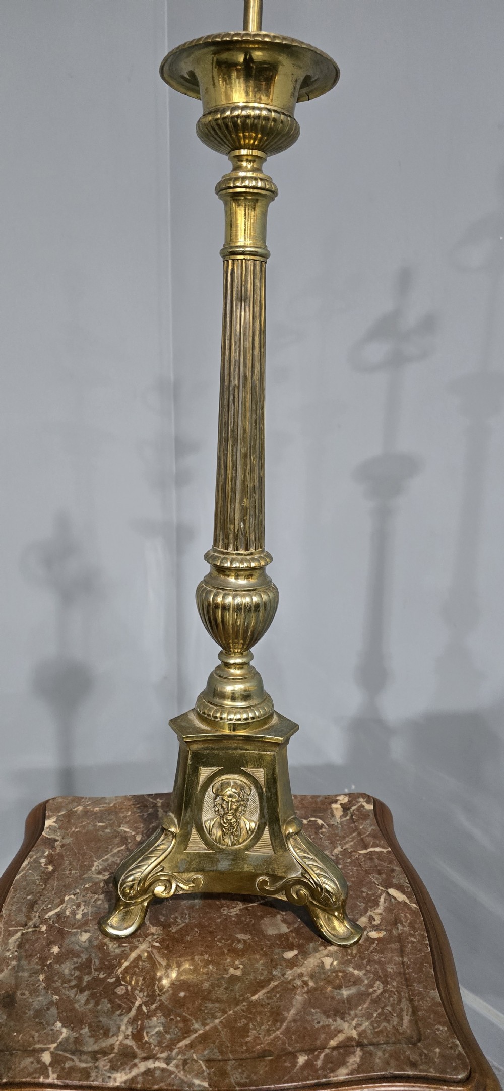 A pair of tall cast brass candlestick table lamps featuring fluted columns, relief portrait medallions on triform bases, and multi-bulb electrical fittings at the top. View V