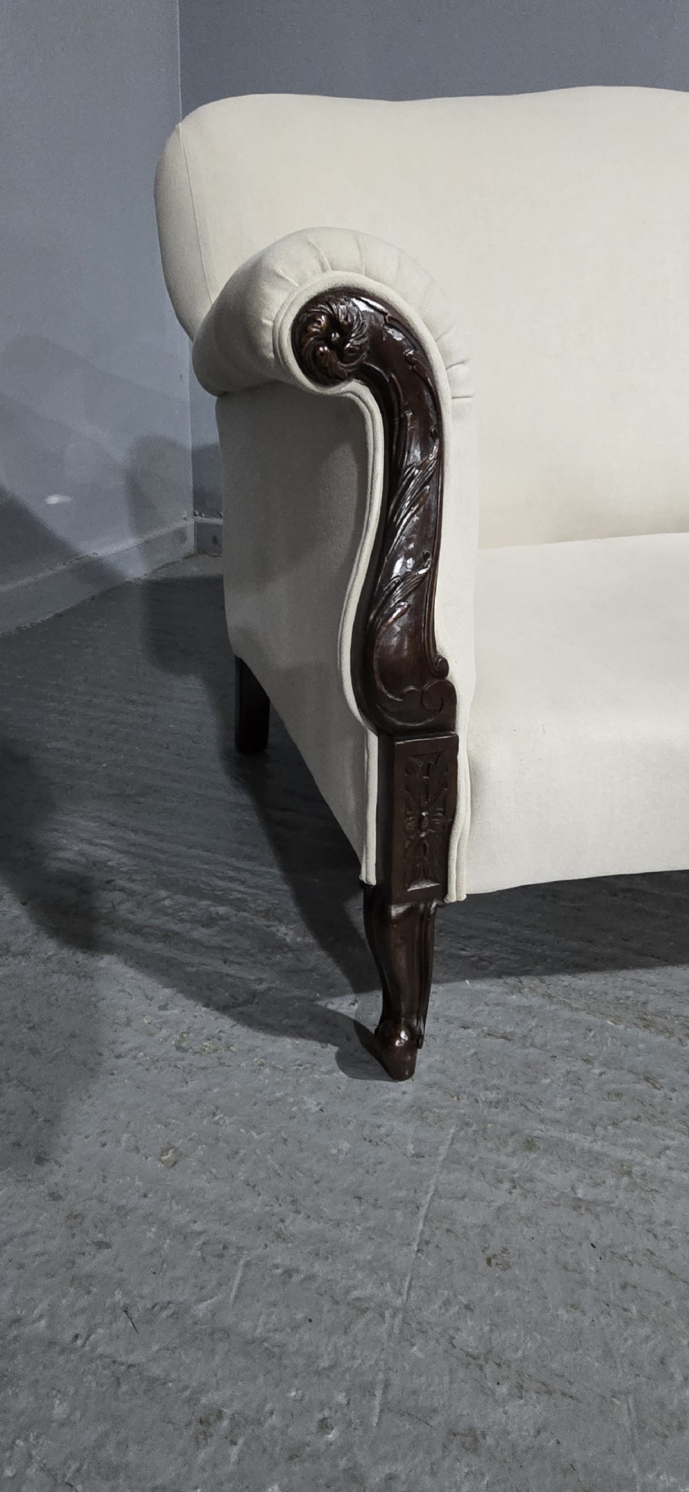 A Victorian two-seater sofa upholstered in plain cream fabric featuring an arched back, rolled padded arms, and dark carved mahogany front legs. View II