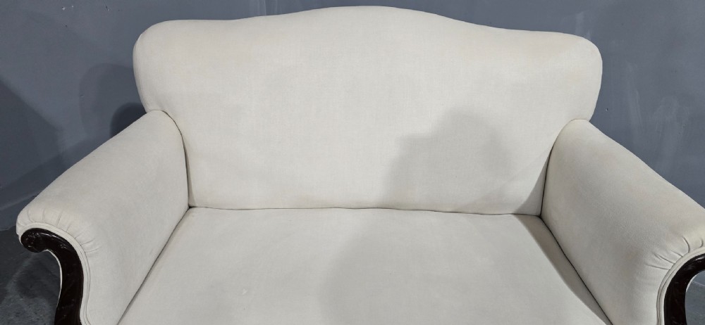 A Victorian two-seater sofa upholstered in plain cream fabric featuring an arched back, rolled padded arms, and dark carved mahogany front legs. View VIII