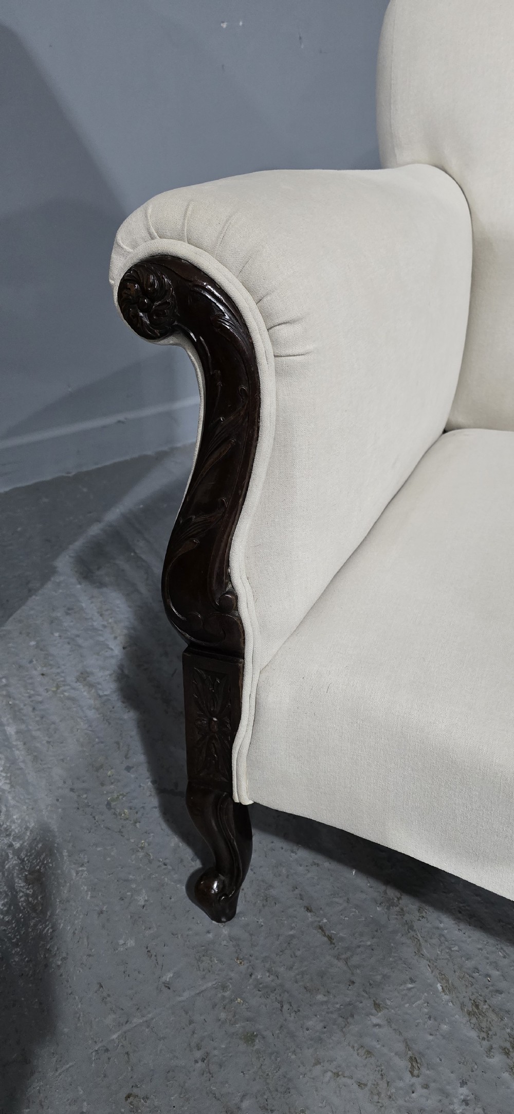 A Victorian two-seater sofa upholstered in plain cream fabric featuring an arched back, rolled padded arms, and dark carved mahogany front legs. View IX