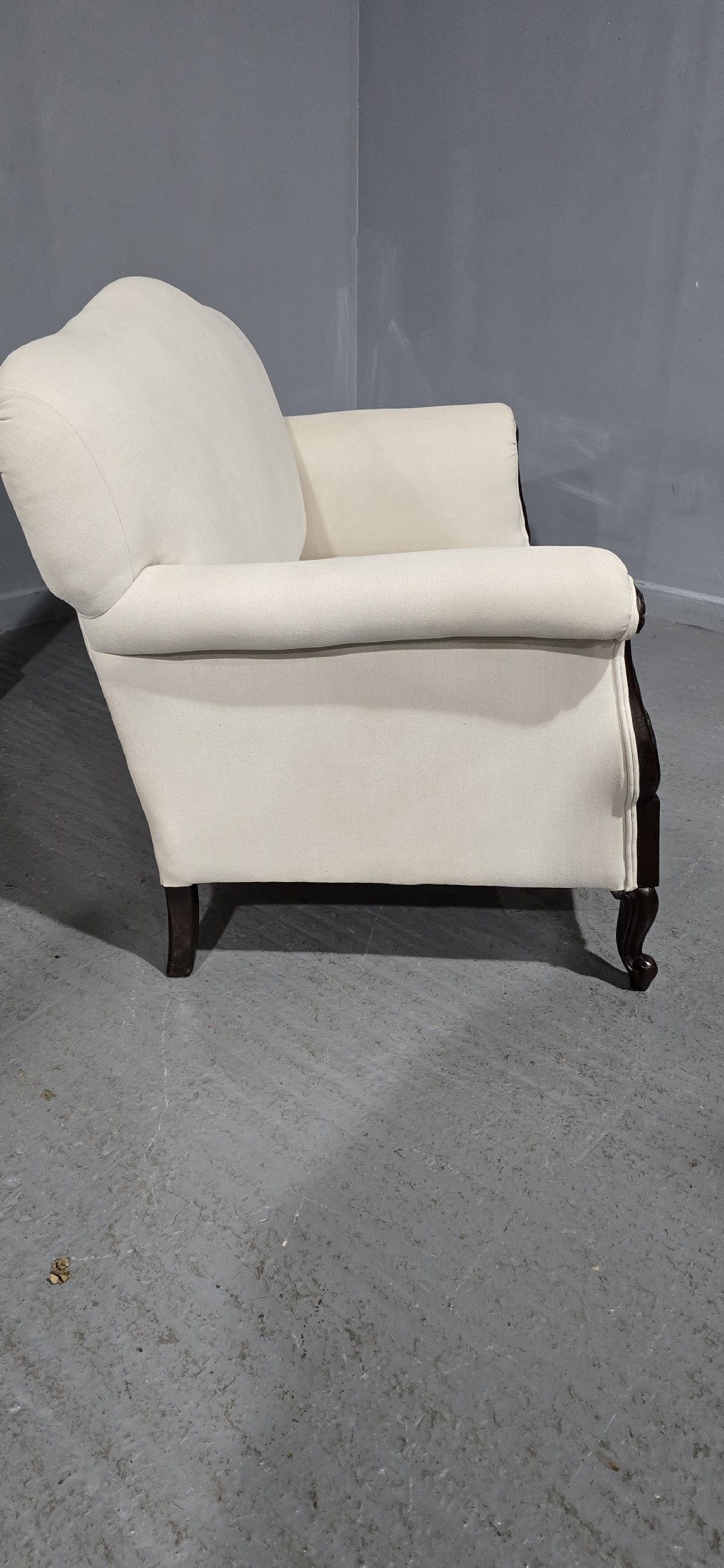 A Victorian two-seater sofa upholstered in plain cream fabric featuring an arched back, rolled padded arms, and dark carved mahogany front legs. View X