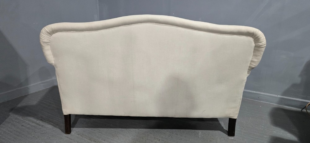 A Victorian two-seater sofa upholstered in plain cream fabric featuring an arched back, rolled padded arms, and dark carved mahogany front legs. View XI