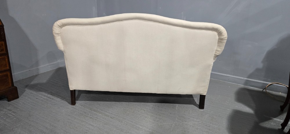A Victorian two-seater sofa upholstered in plain cream fabric featuring an arched back, rolled padded arms, and dark carved mahogany front legs. View XII
