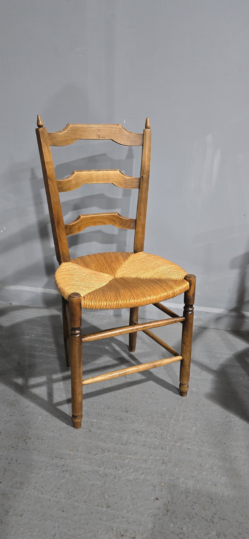 A set of eight French country wooden dining chairs featuring wavy ladderback rails and natural woven rush seats. View III