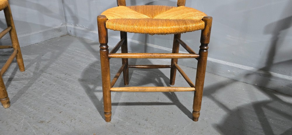 A set of eight French country wooden dining chairs featuring wavy ladderback rails and natural woven rush seats. View IV