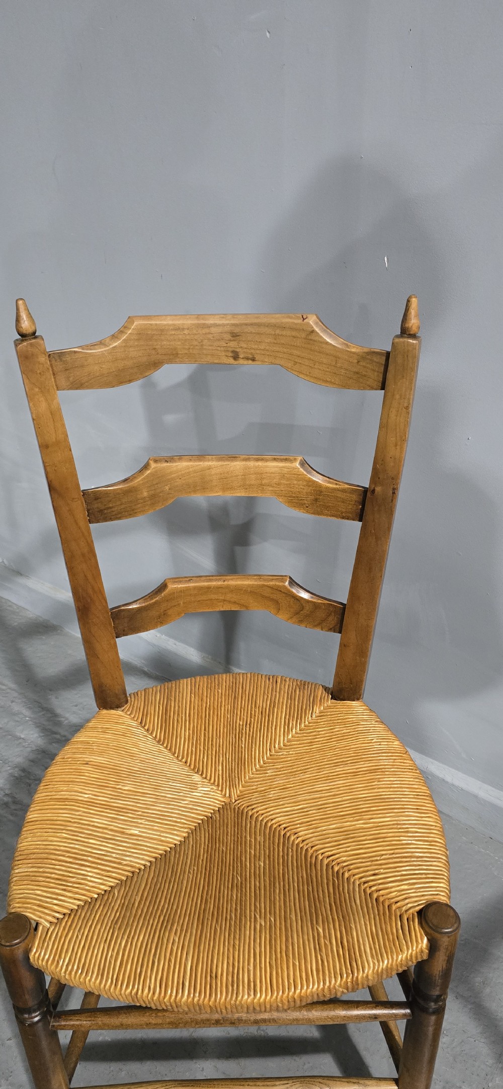 A set of eight French country wooden dining chairs featuring wavy ladderback rails and natural woven rush seats. View VI