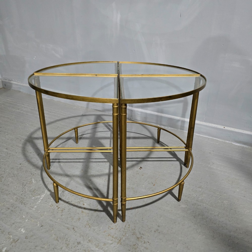 A set of four quadrant-shaped gold brass tables with glass tops arranged together to form a single circular surface.