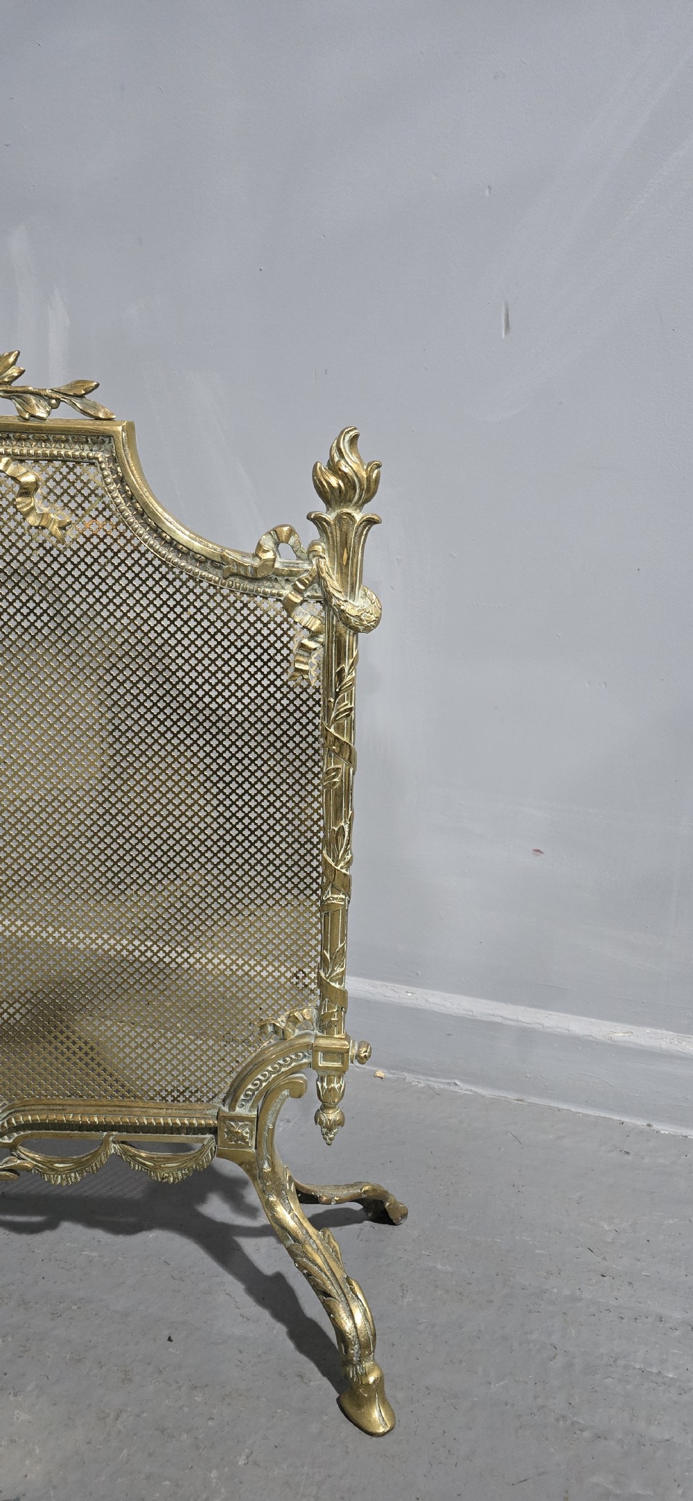 A Victorian gilt brass fire guard featuring a fine mesh panel, ribbon garlands, top wreath crest, and ornate torch finials. View III